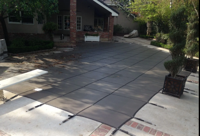 Brick driveway with large gray pavers in front of a house, bordered by trees and planters