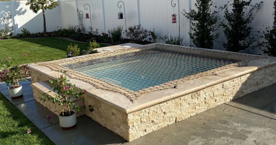 Raised stone pool with blue water and potted plants in a sunny courtyard