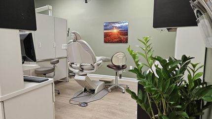 Dental clinic room with chair, equipment, cabinets, and a potted plant in the foreground