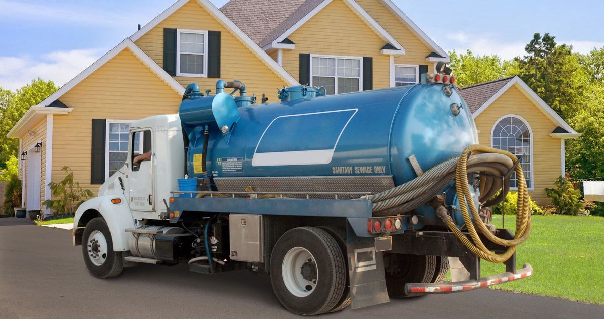 A blue septic tank truck parked in the driveway of a yellow two-story house.