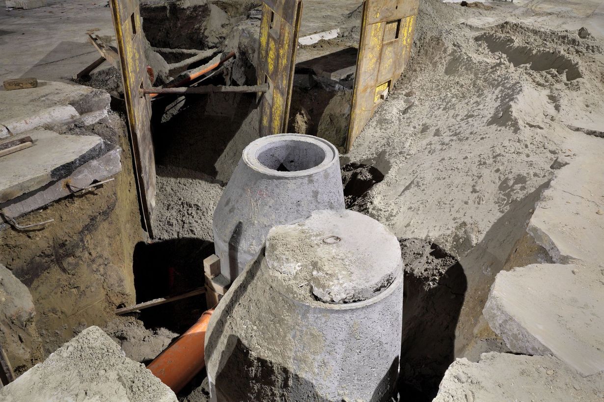 Construction site with concrete cylinders in a dug trench, surrounded by dirt and debris.