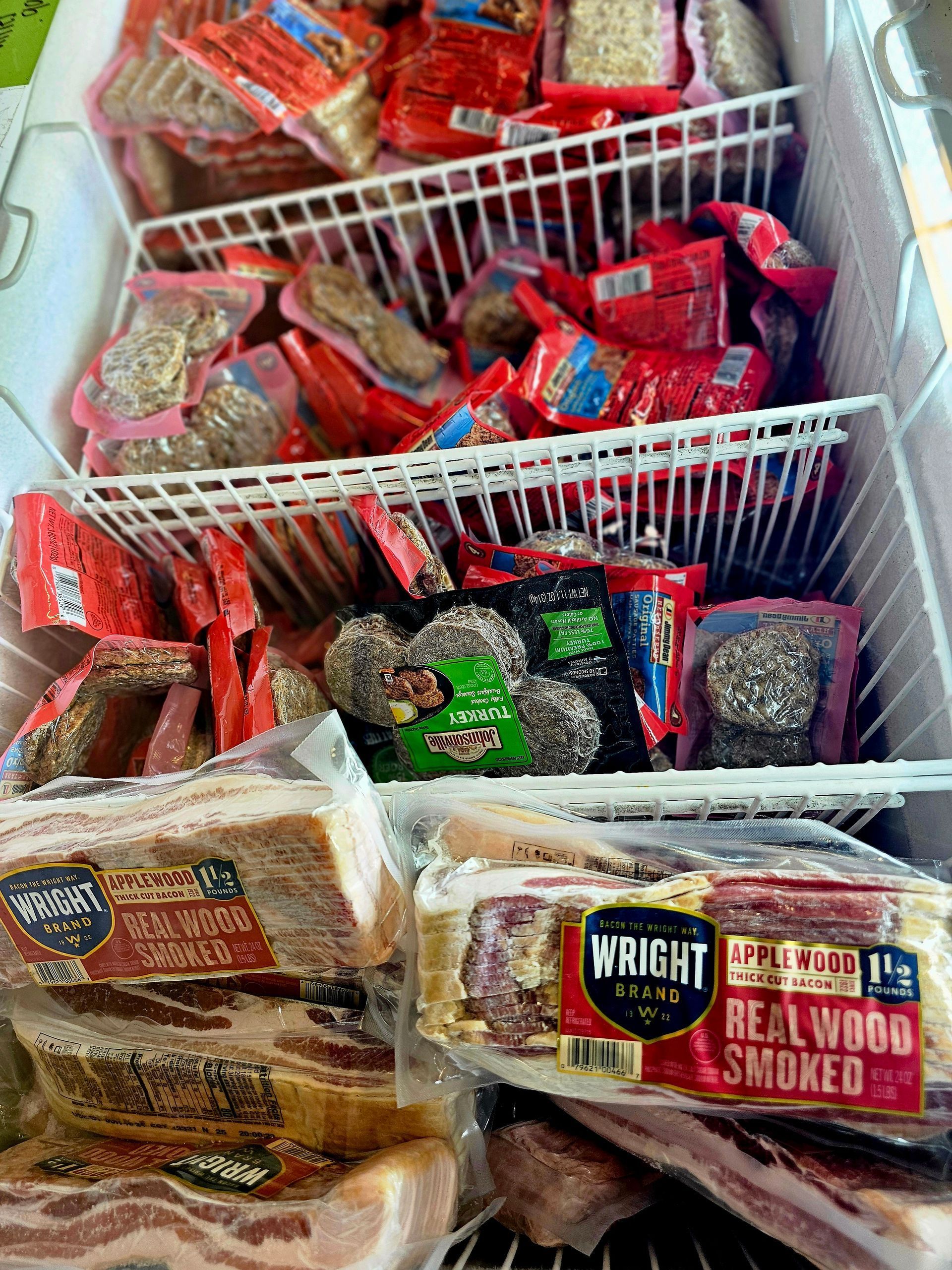 A freezer filled with a variety of meats including bacon and sausage.