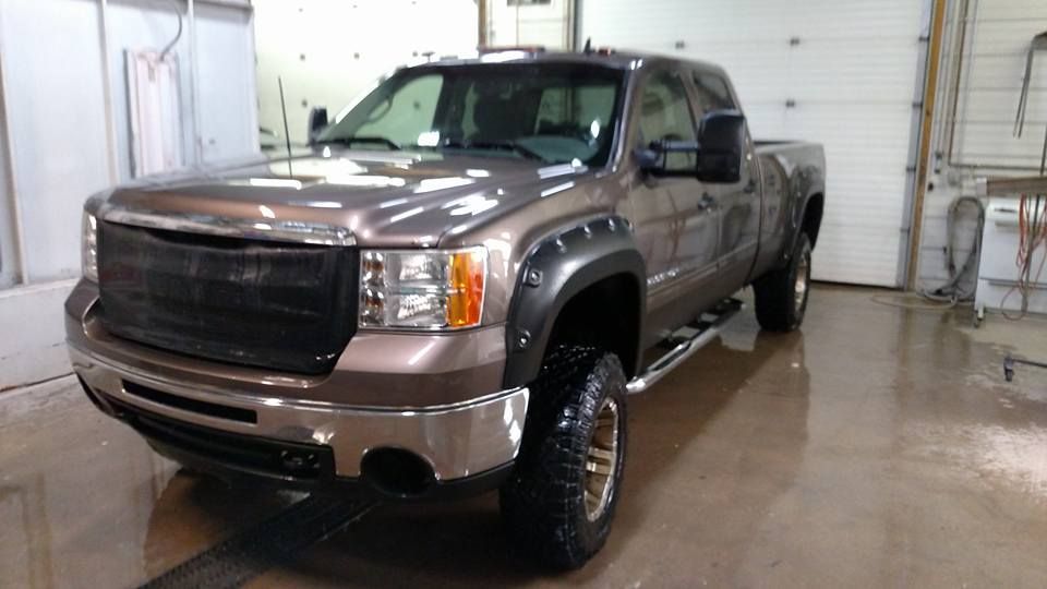 Brown pickup truck with black grill and fender flares, in a wash bay.