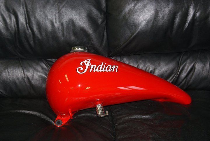 Red Indian motorcycle gas tank with chrome Indian script, set on black leather.