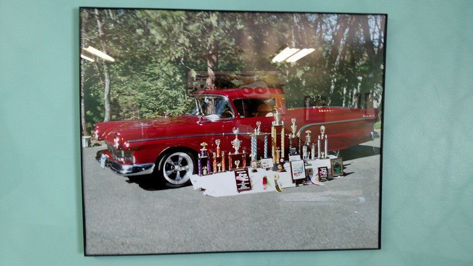 Red vintage pickup truck with many trophies displayed in front of it.