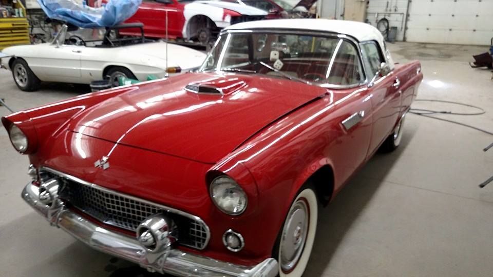 Red vintage Ford Thunderbird convertible with a white top in a garage.