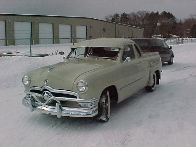 Cream-colored vintage pickup truck parked in the snow in front of a building.