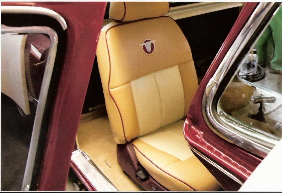 Tan and cream leather car seat with red trim, inside a classic car with an open door.