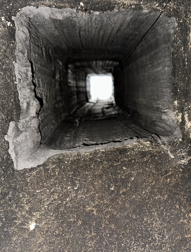 Inside view of a narrow square concrete chimney or ventilation shaft leading to a bright opening above