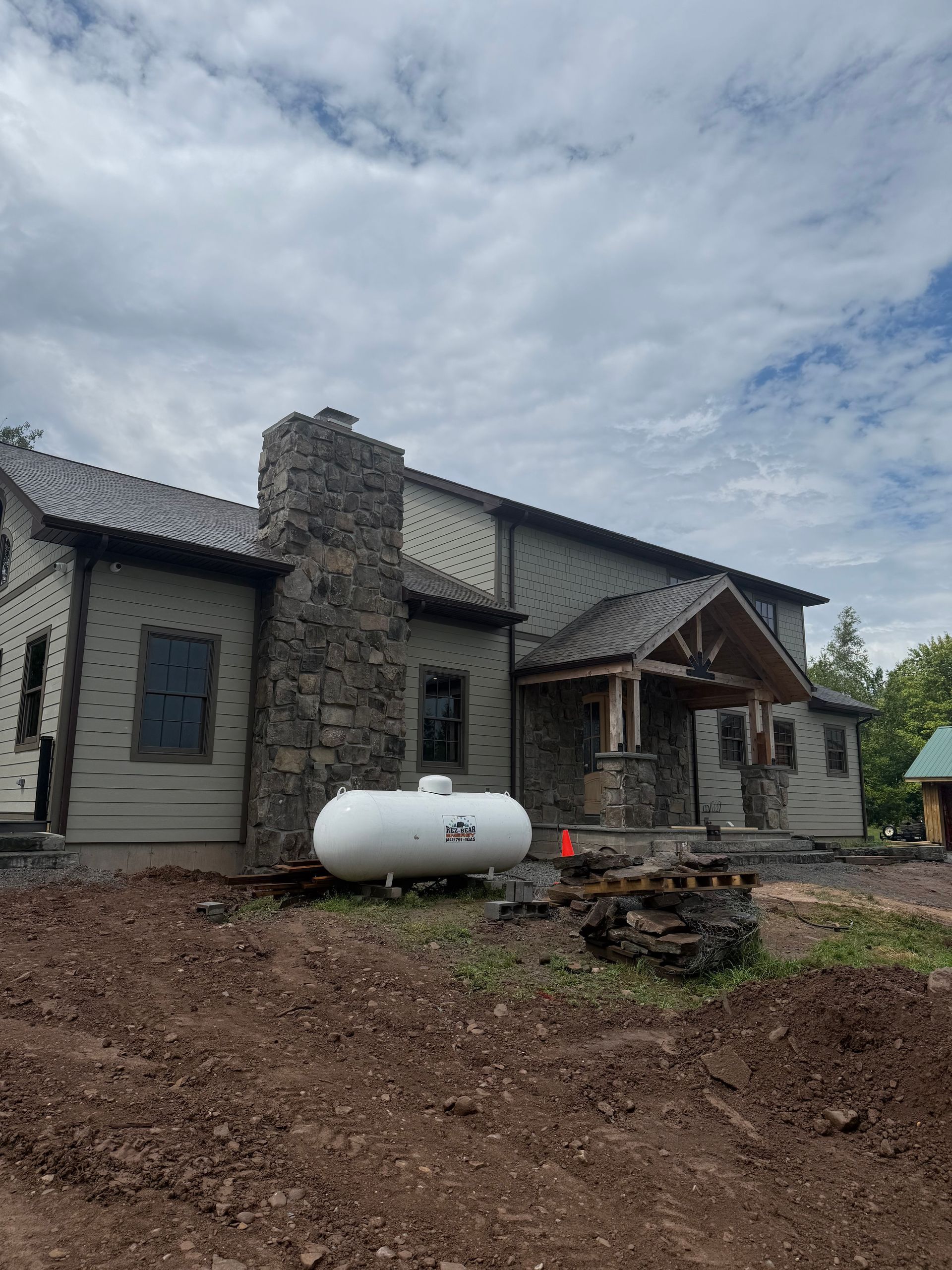 Stone house under construction with a white propane tank in front and muddy ground
