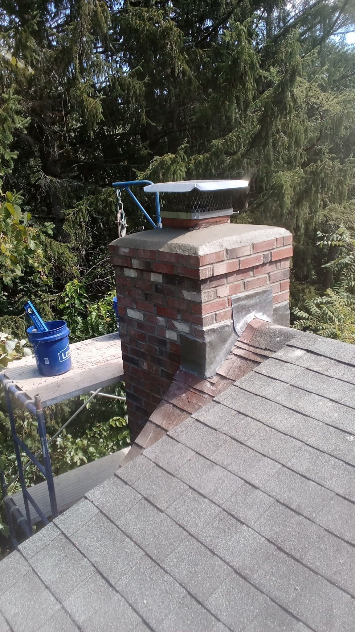 Brick chimney on a shingled roof with trees in the background