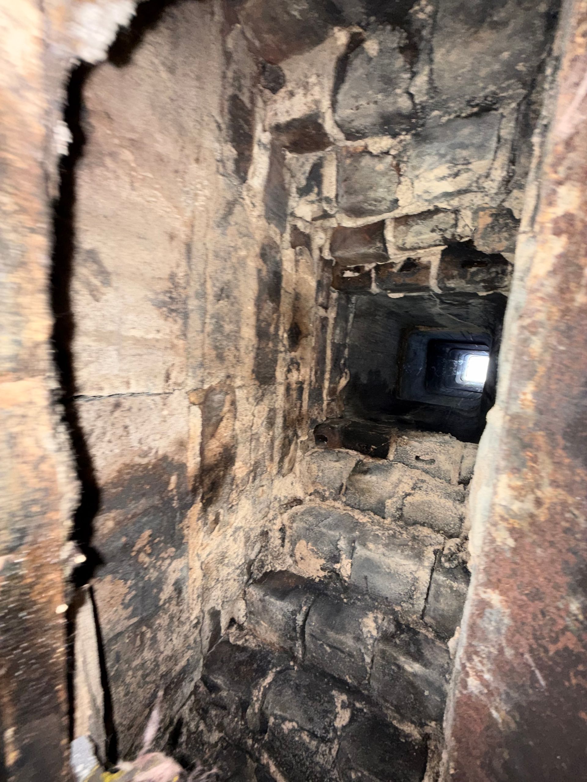 Narrow, soot-stained brick chimney or tunnel with a bright opening at the far end