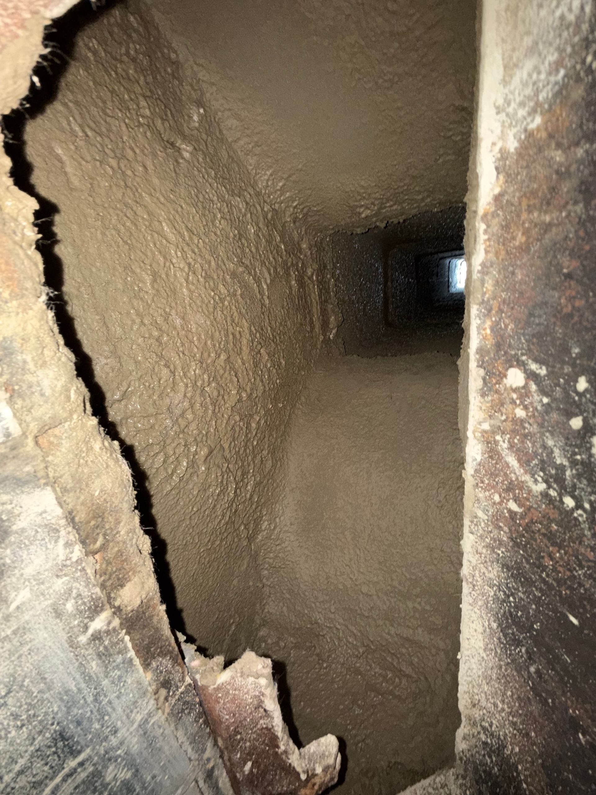 Close-up of a rusted metal pipe interior with a jagged opening and dark tunnel-like view inside