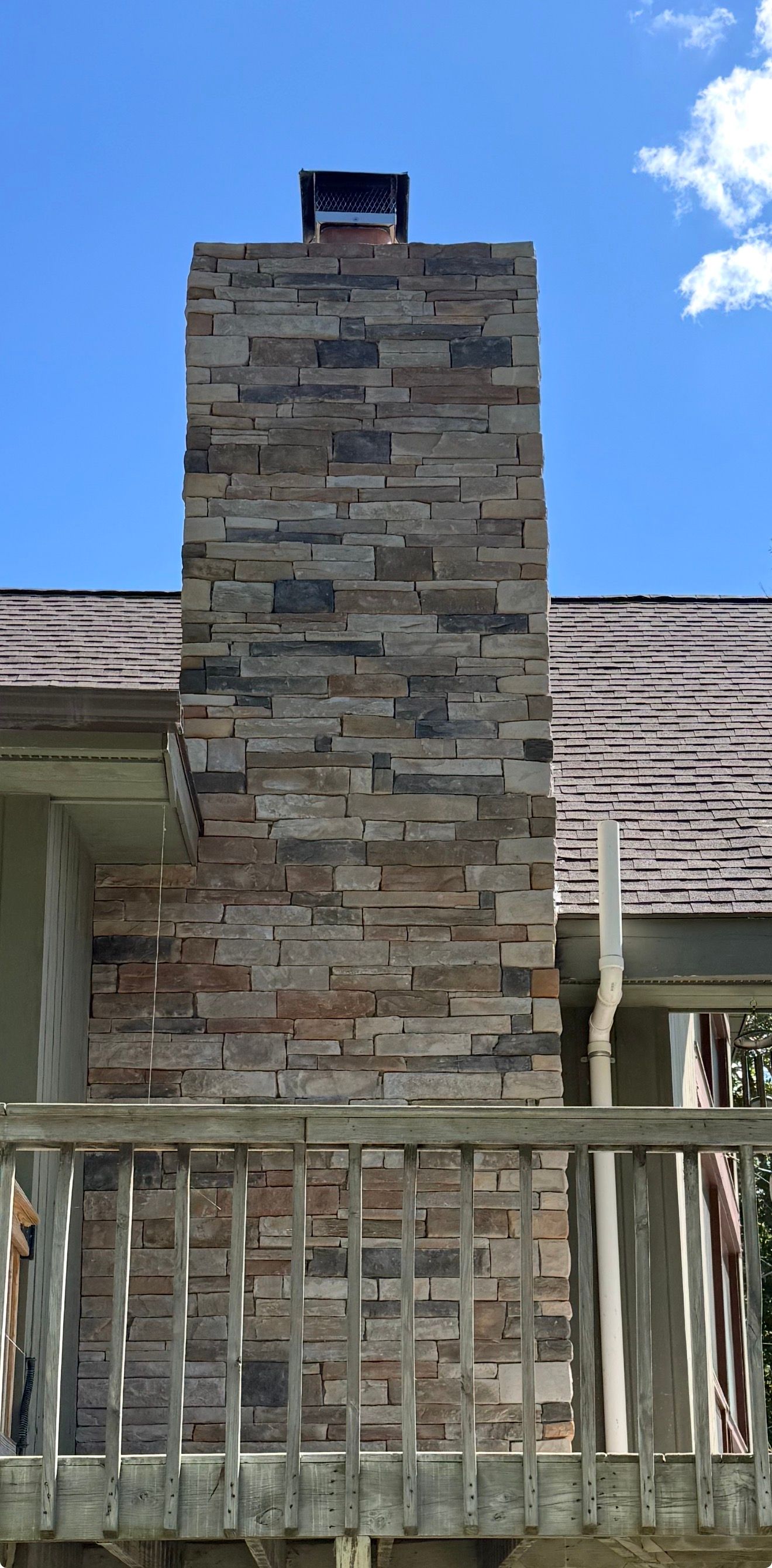 Stone chimney on a house porch beneath a blue sky, with a white railing in front