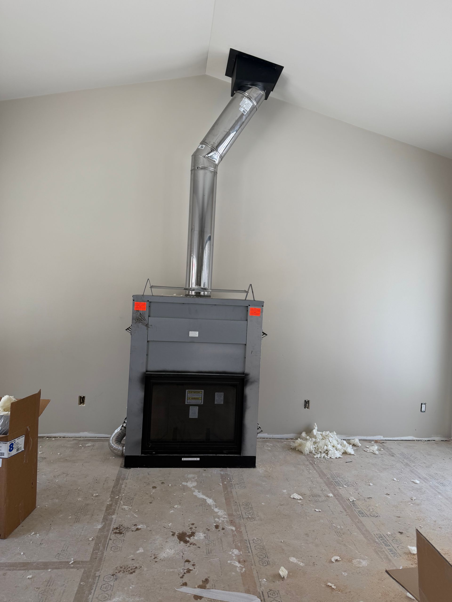 Large black furnace with silver ductwork in a nearly empty room under renovation.
