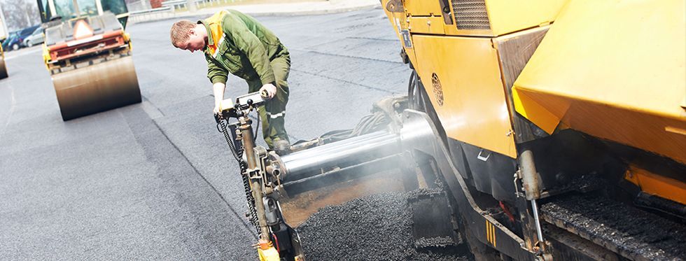 Worker operating asphalt paver machine during road construction