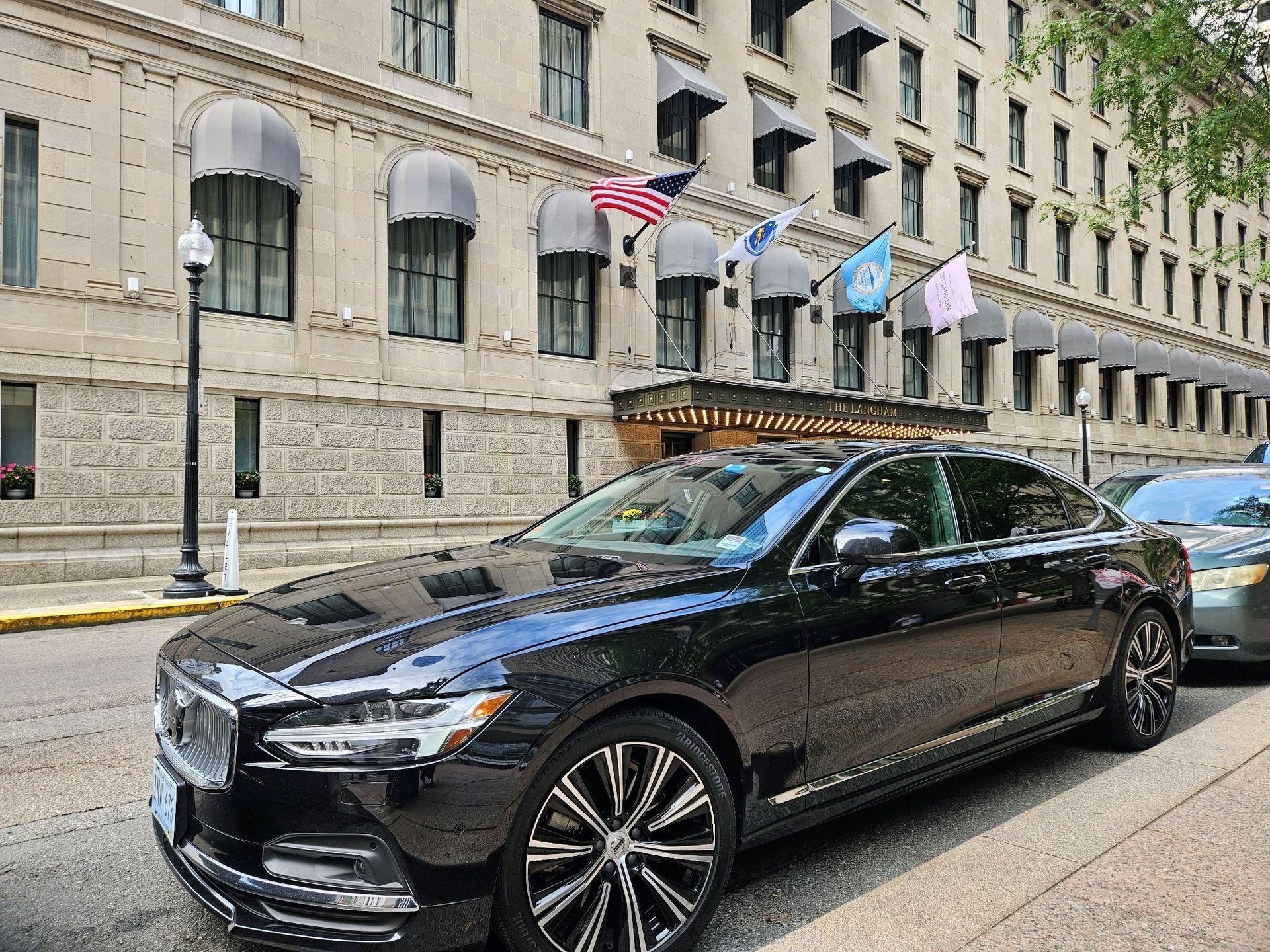 Black Volvo sedan parked in front of an old building with flags.