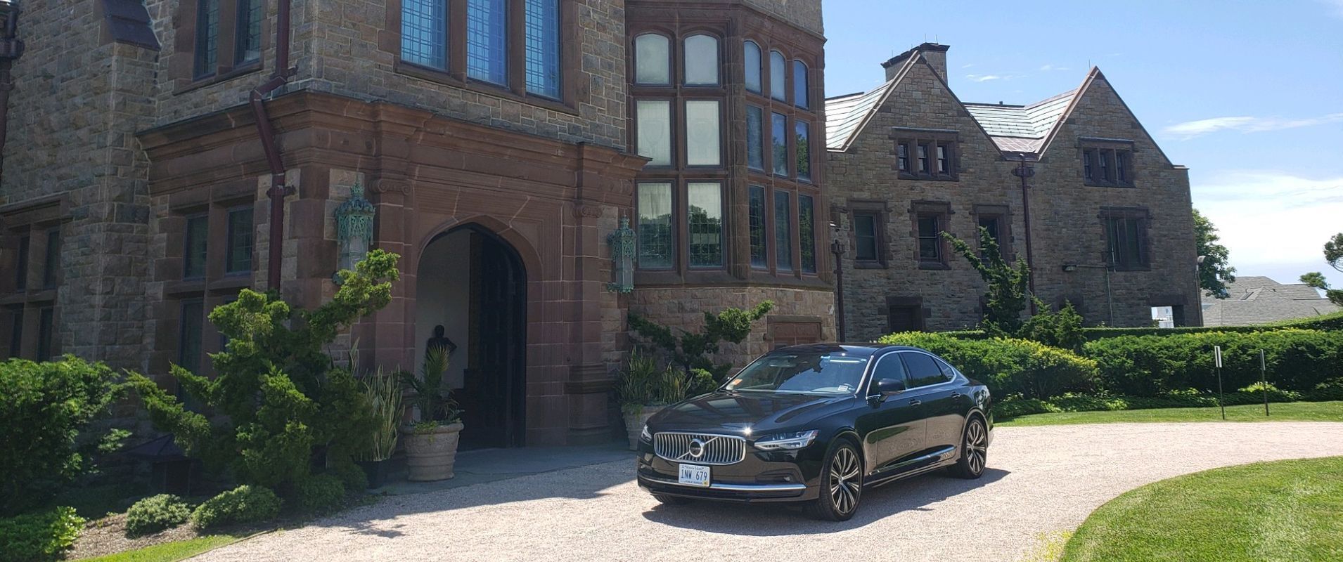 Black car parked in front of a stone mansion with a circular driveway.