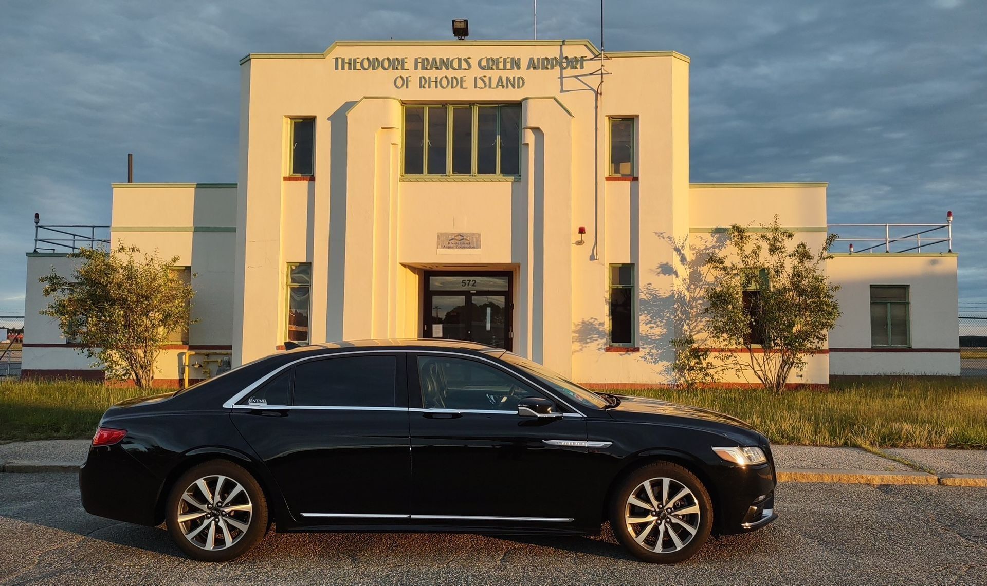 Black Lincoln Continental parked in front of a light-colored art deco building.