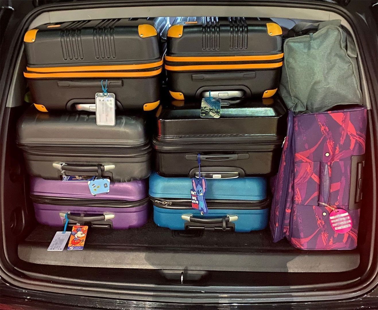 Trunk of a car packed with various suitcases, in black, blue, purple, and with orange accents.