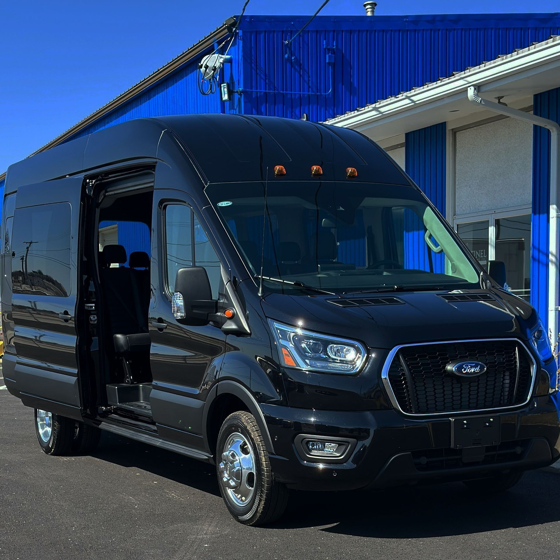 Black passenger van parked on asphalt in front of a blue building.