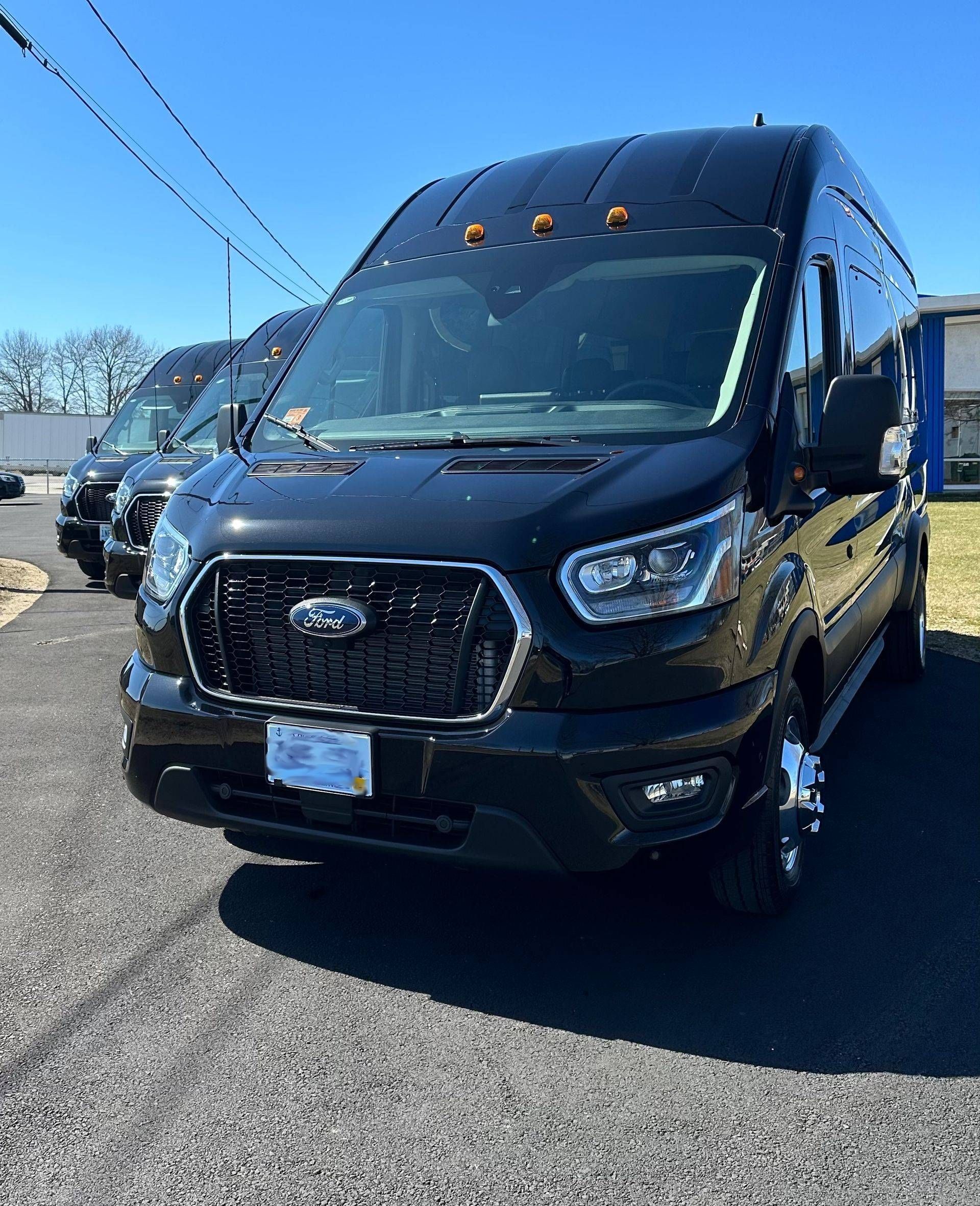 Black Ford Transit van parked outside on a sunny day. Another van is partially visible behind it.