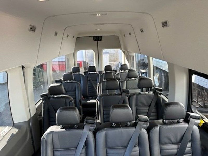 Interior view of a passenger van with multiple rows of black seats and seatbelts.