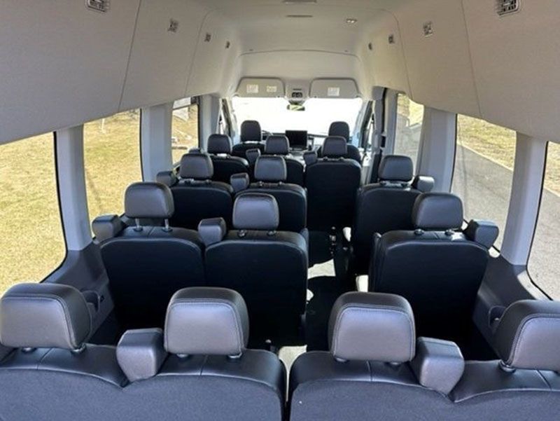 Interior view of a passenger van with black seats arranged in rows. Windows line both sides.