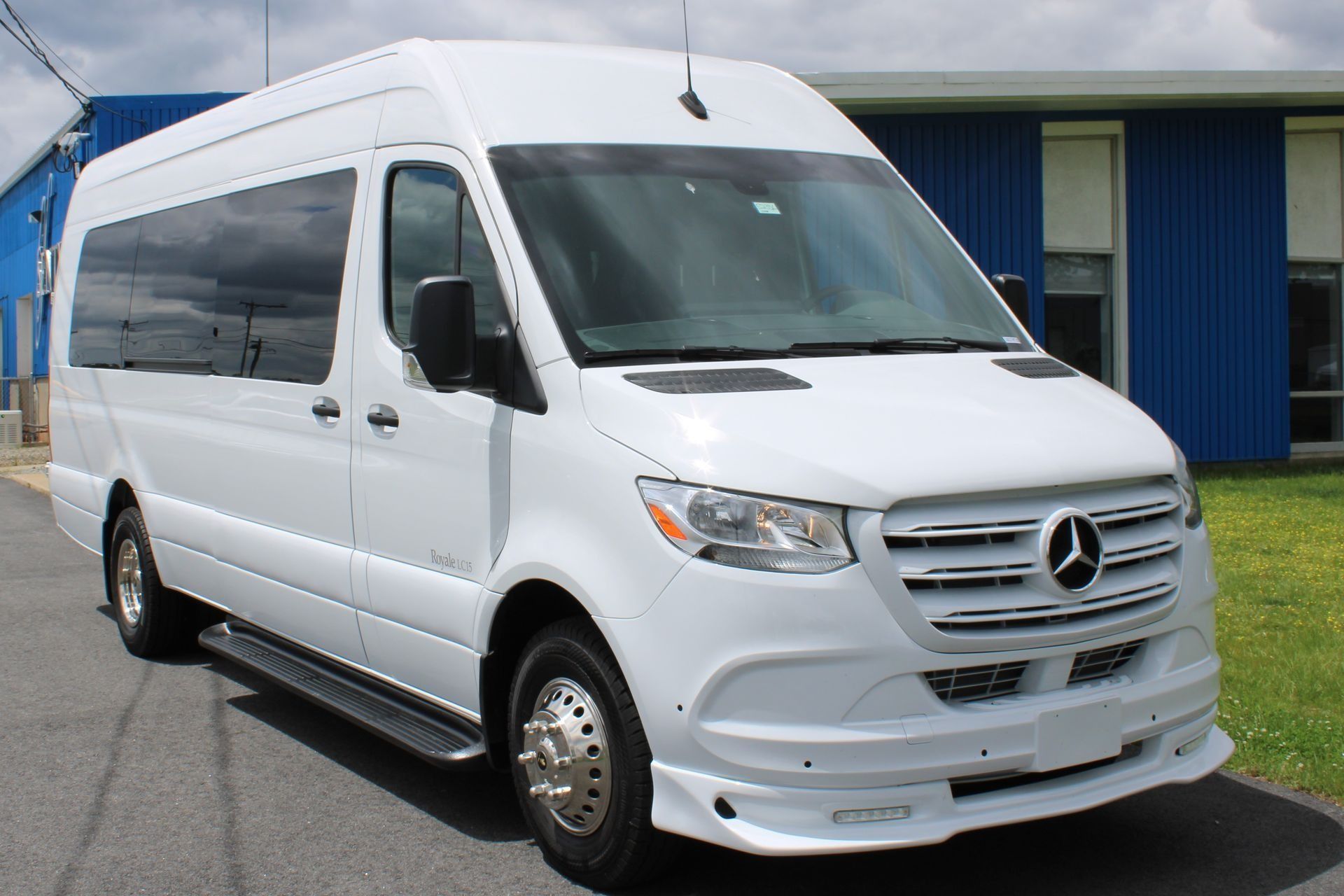 White Mercedes Sprinter van parked outdoors in front of a blue building.