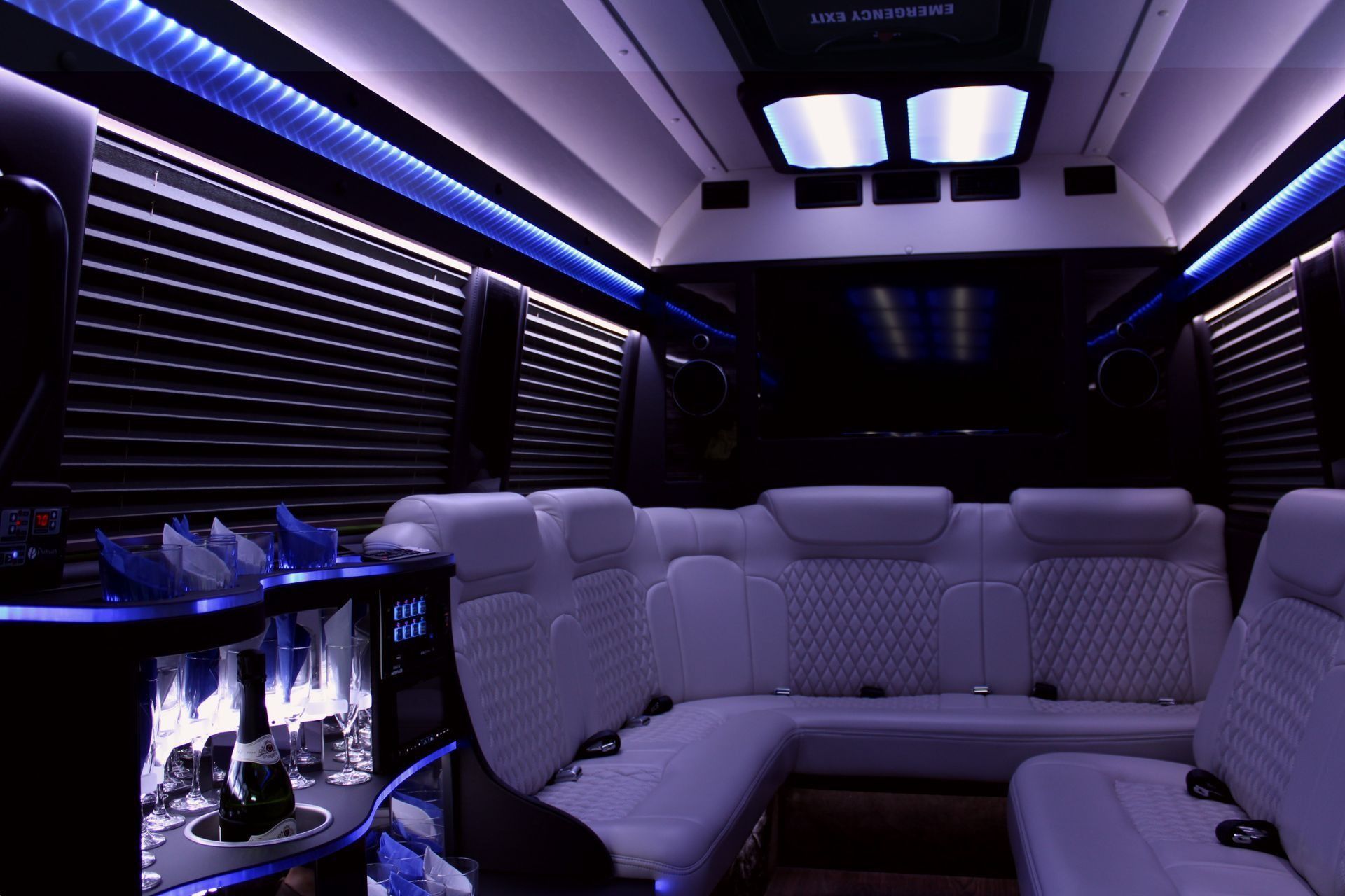 Interior of a luxury passenger van with white seating and blue mood lighting.