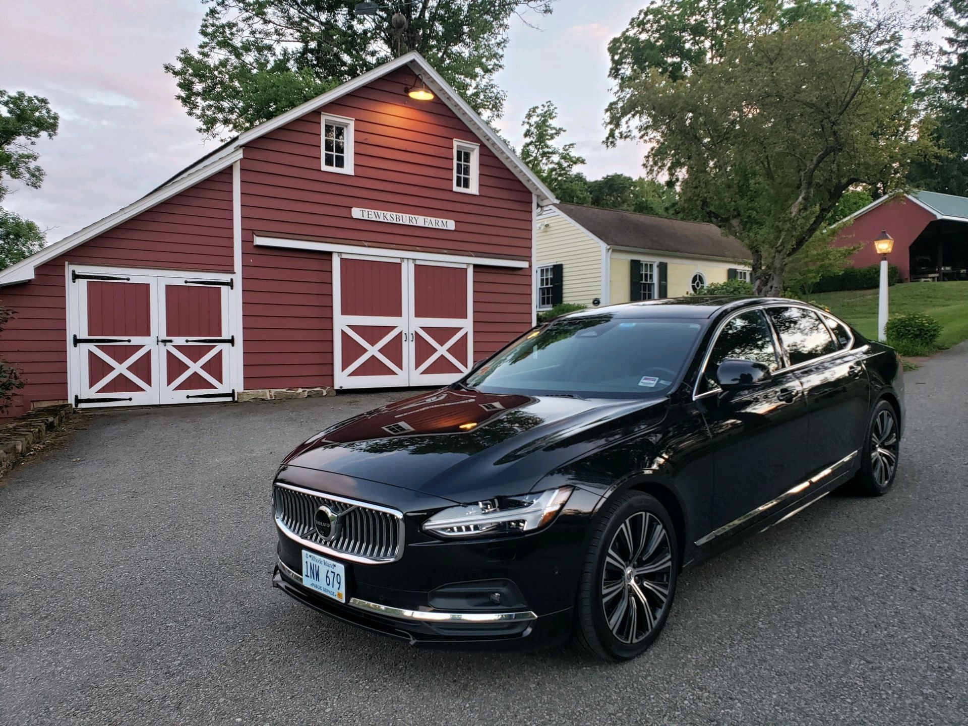 Black Volvo sedan parked in front of a red barn with white doors, set in a rural landscape.