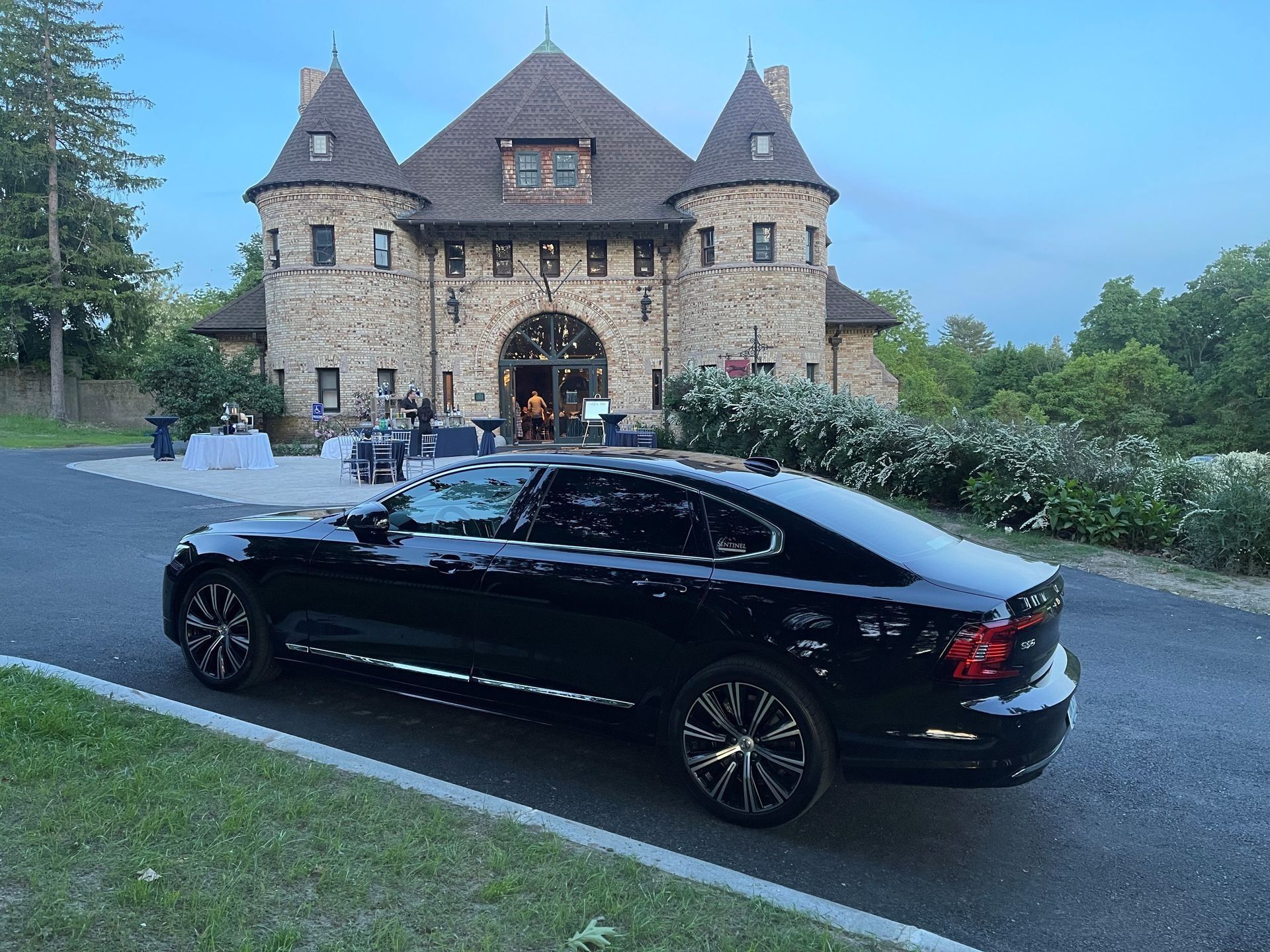 Black car parked in front of a stone castle-like building with turrets; evening setting.