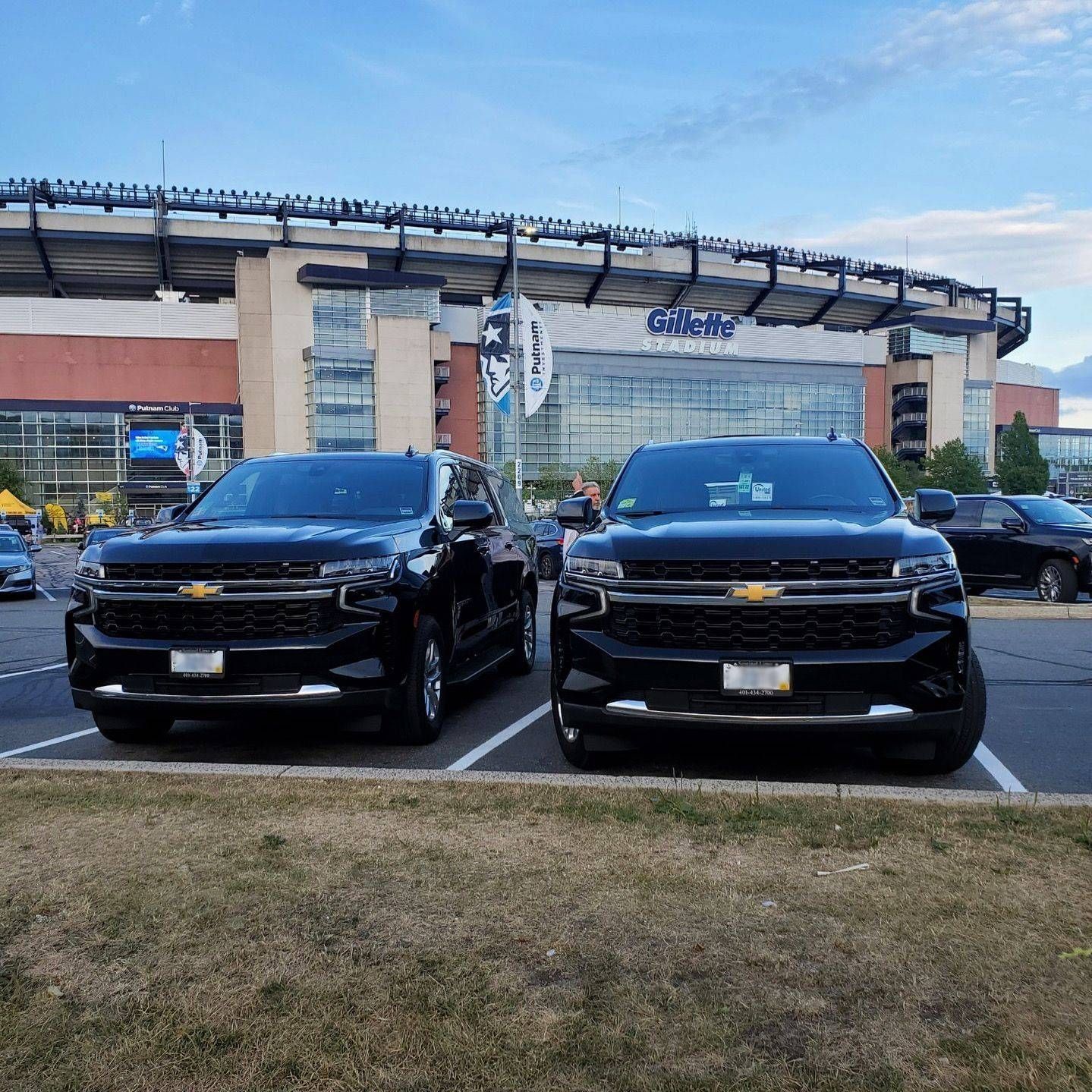 Two black SUVs parked in front of a large stadium under a blue sky.
