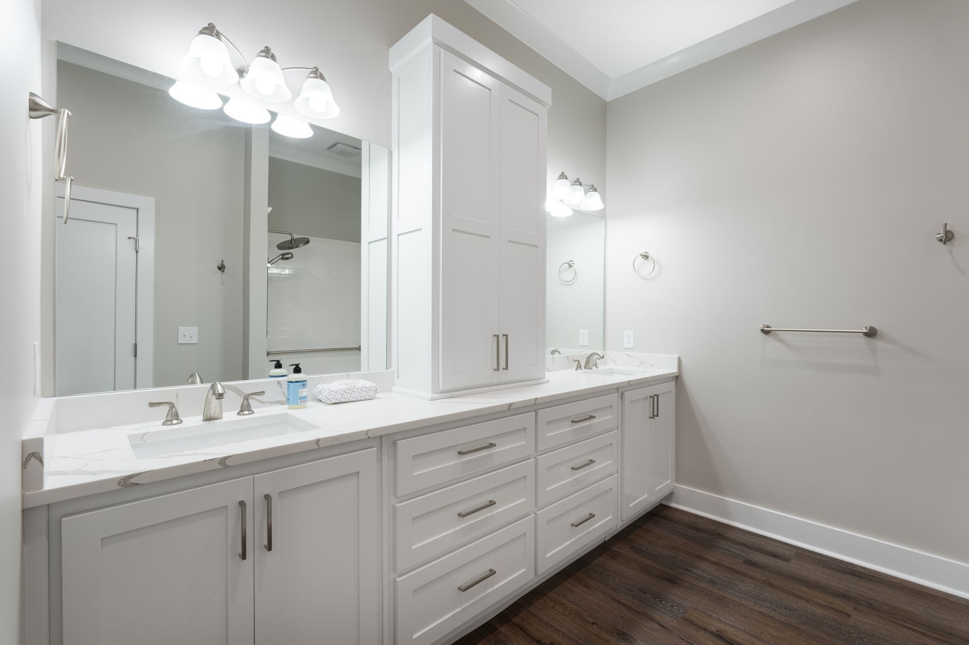 Bright modern bathroom with double vanity, white cabinets, large mirror, and dark wood floor