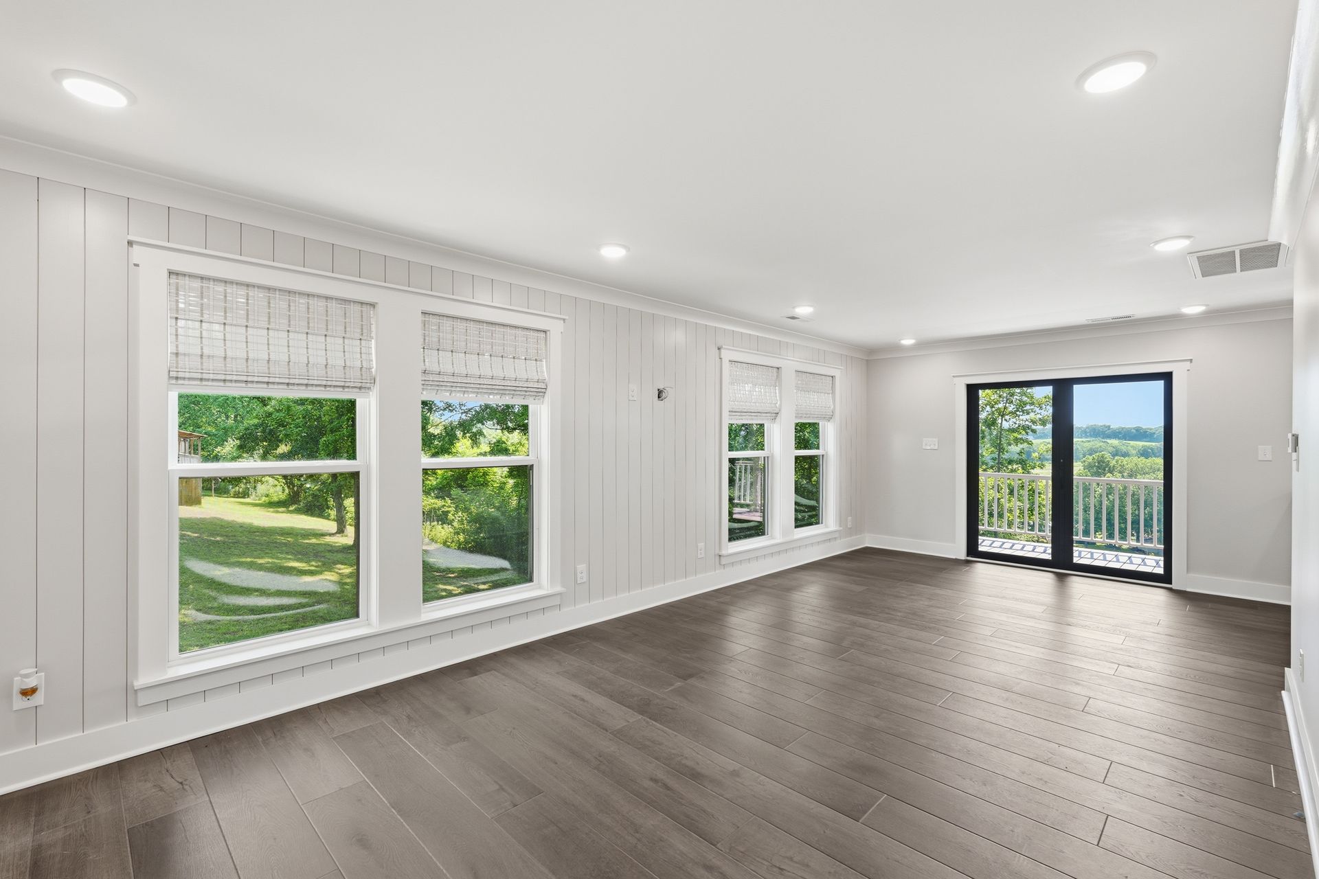 Bright empty living room with white walls, wood floors, large windows, and sliding glass doors to a balcony