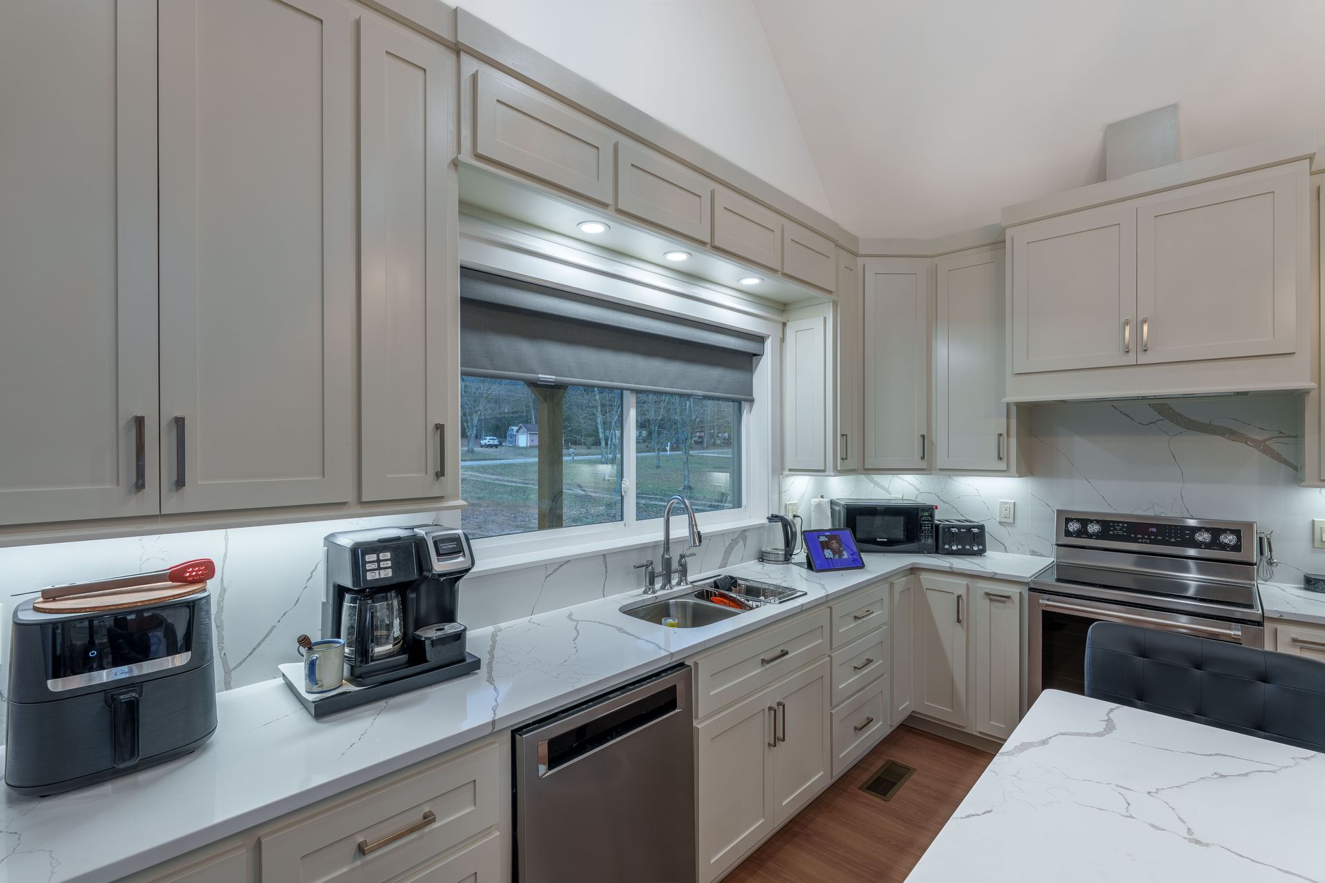 Modern white kitchen with stainless appliances, island, and large window above the sink