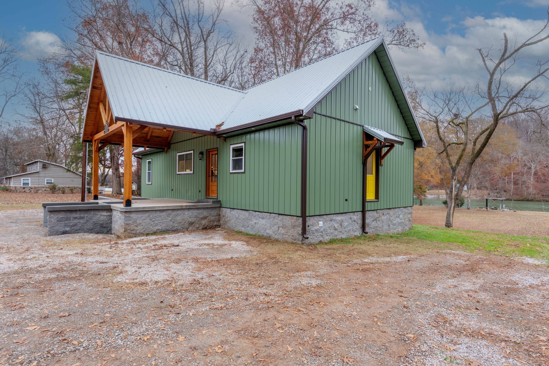 Small green cabin with a covered porch and metal roof in a leafless wooded clearing