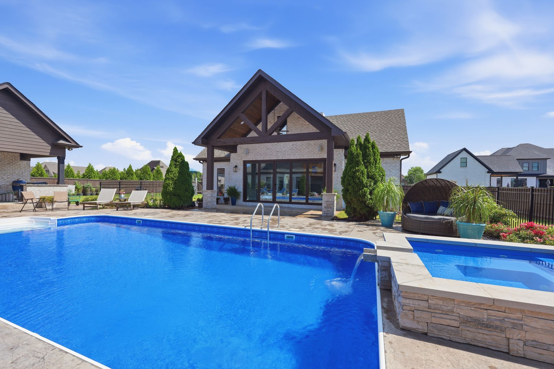 Backyard swimming pool beside a modern house with a covered patio and blue sky