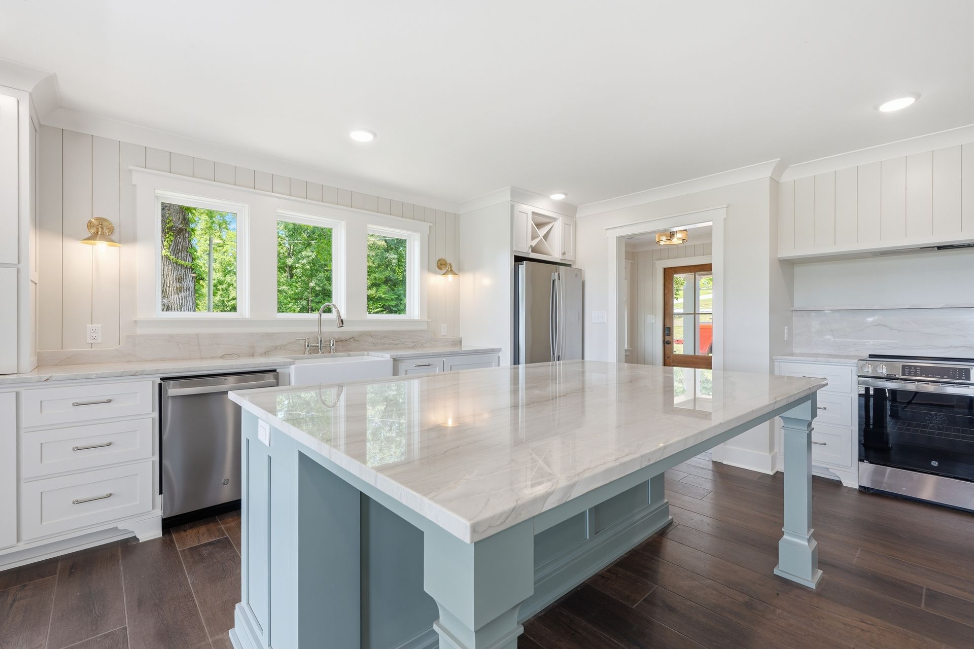 Bright modern kitchen with white cabinets, large island, stainless appliances, and dark wood floors