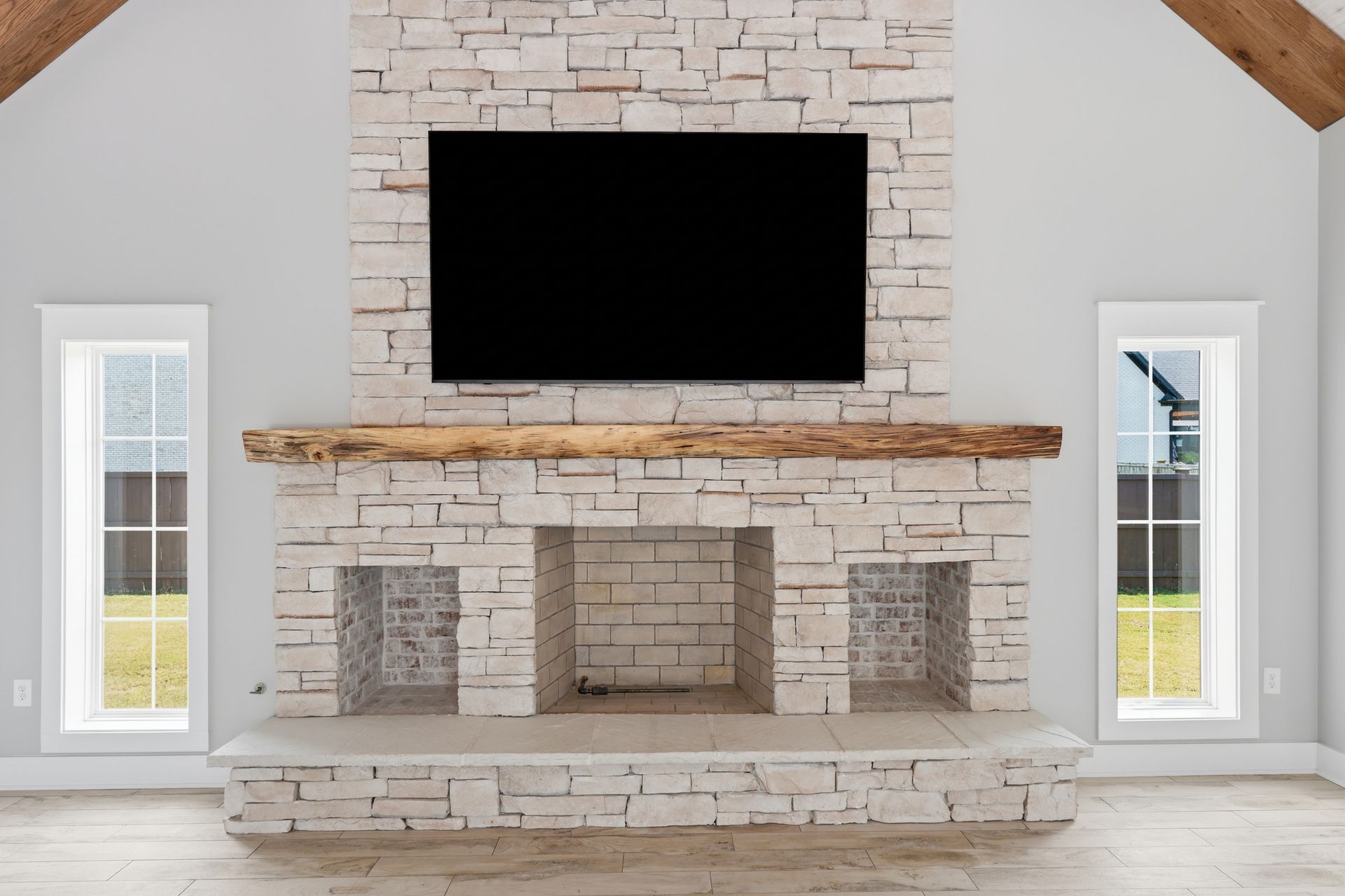 Modern living room fireplace with a mounted TV and stone surround, flanked by tall windows.