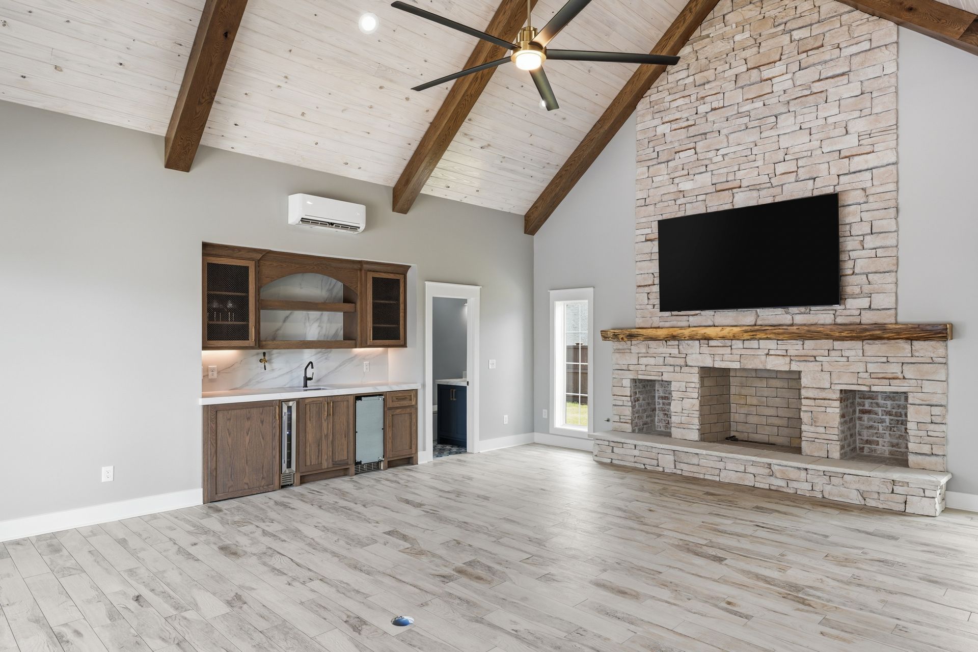 Spacious living room with vaulted ceiling, white brick fireplace, built-in shelves, and light wood floors