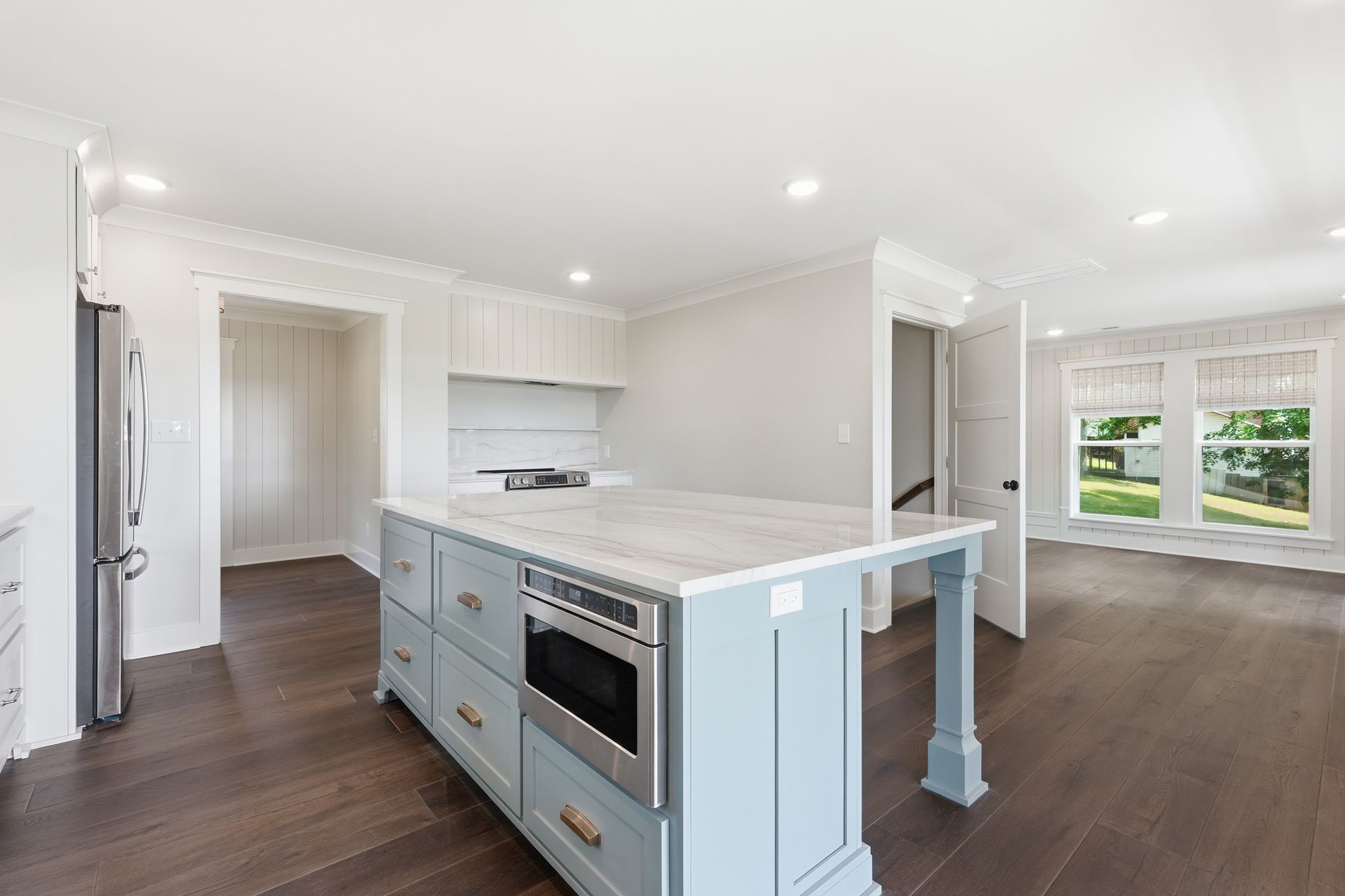 Bright open kitchen and living room with blue island, white cabinets, and large windows