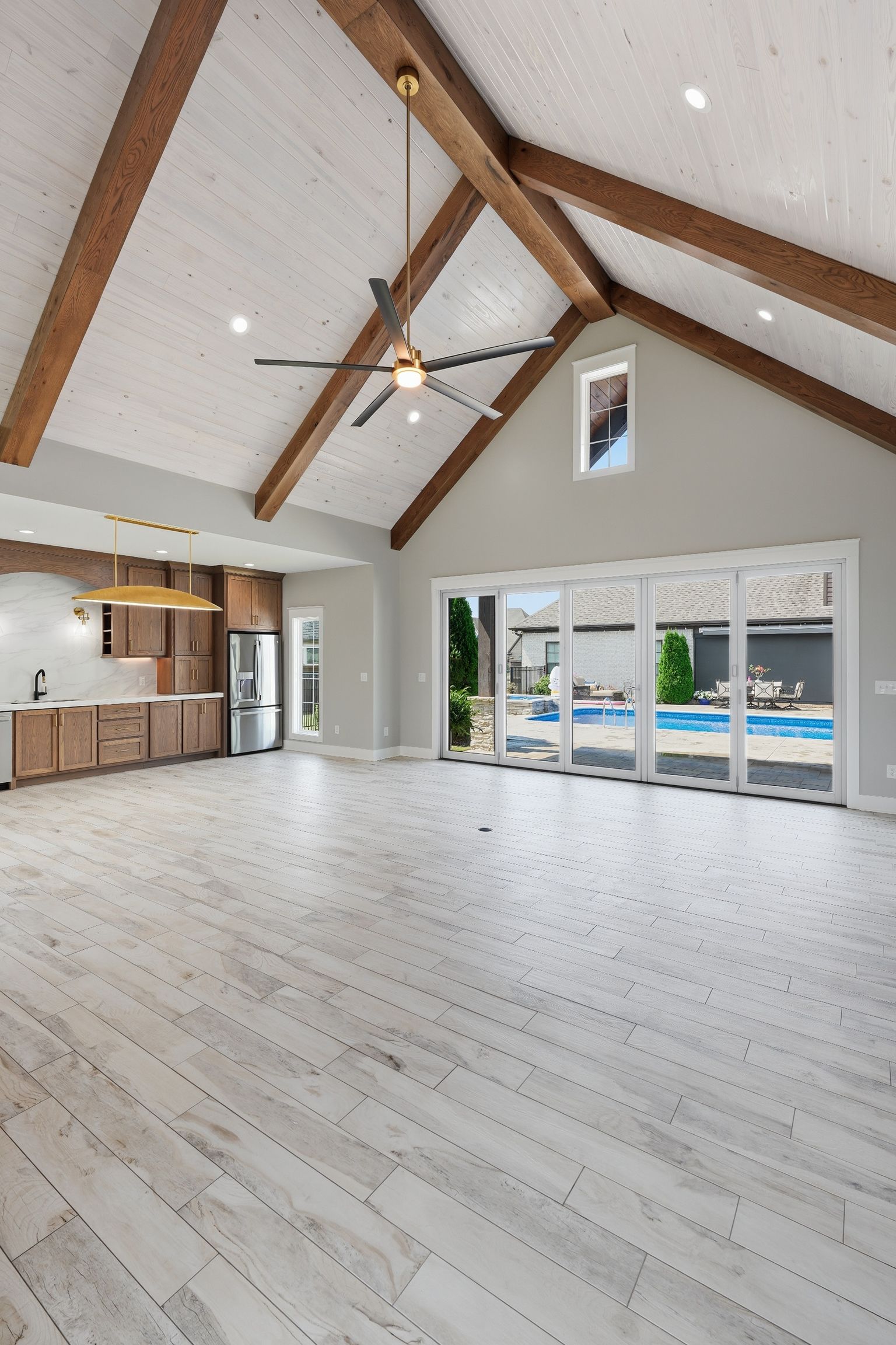 Spacious vaulted living room with wood beams, white floors, and sliding glass doors to a pool patio.