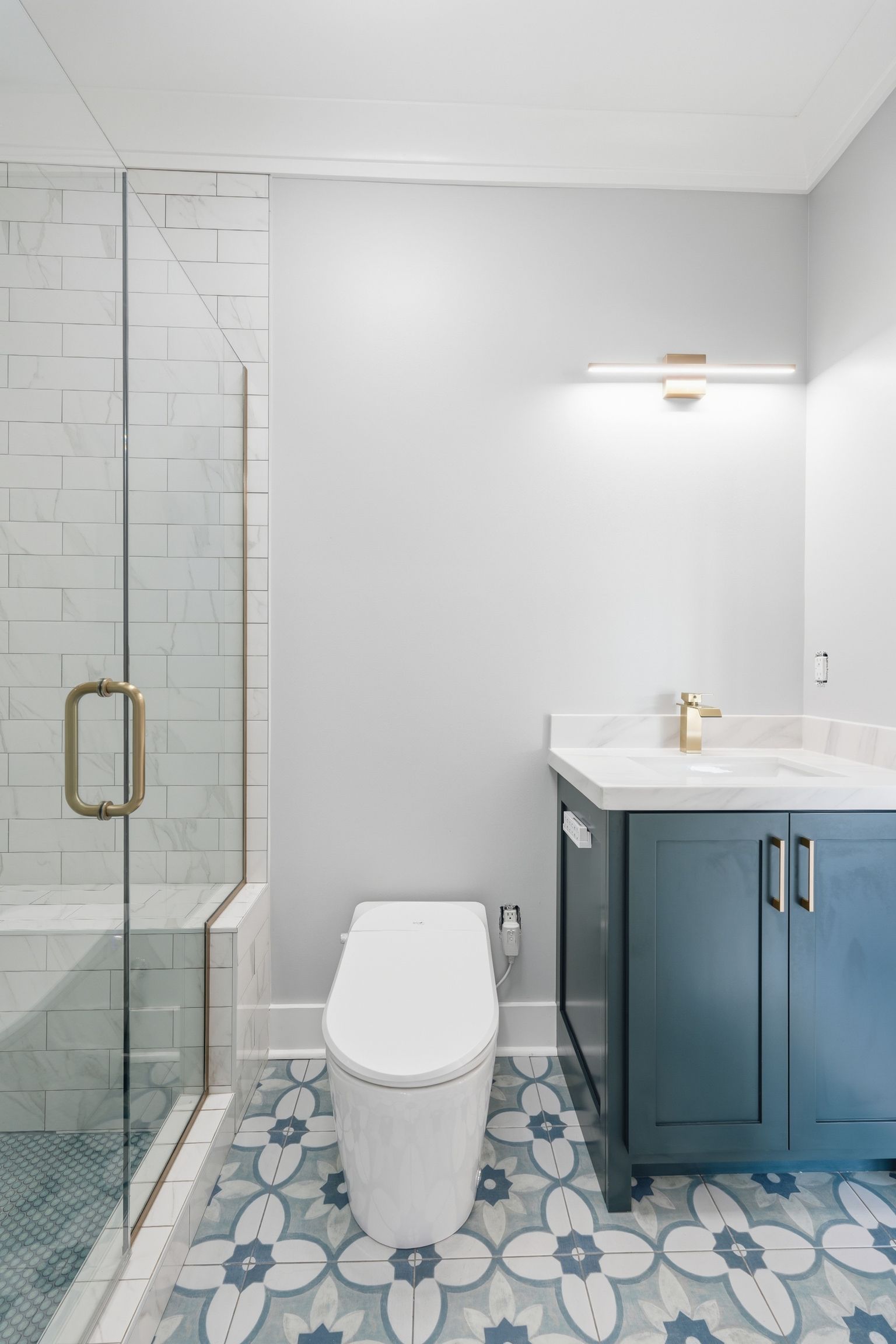 Modern bathroom with glass shower, toilet, and blue vanity on patterned tile floor.