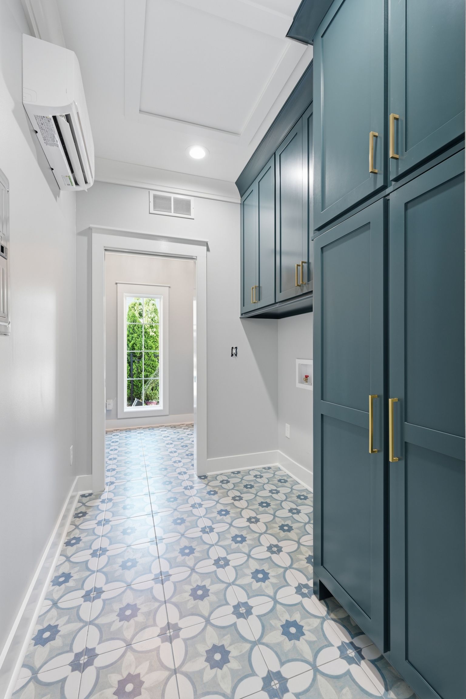 Narrow laundry room with teal cabinets, patterned tile floor, white walls, and a windowed back door.
