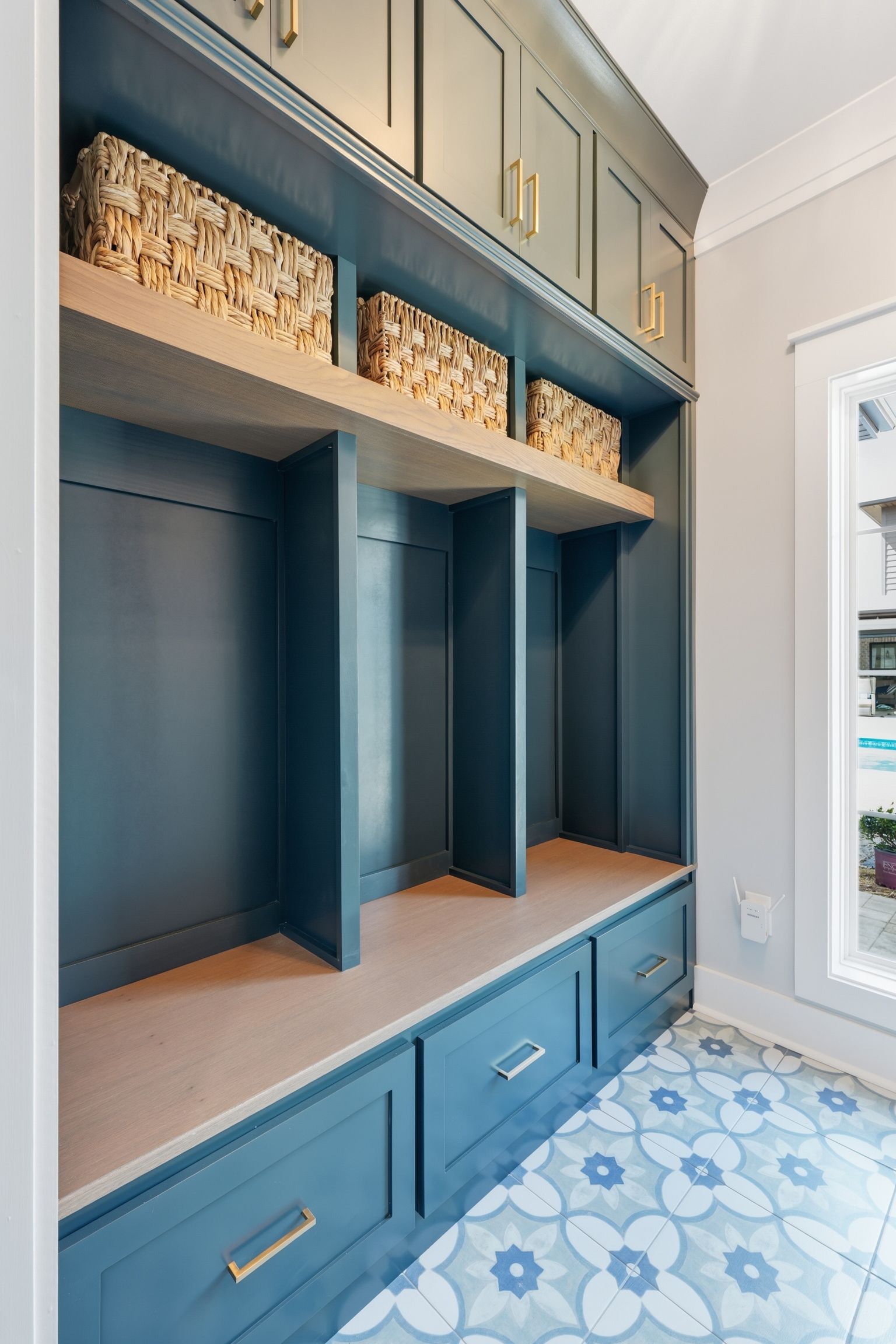 Built-in teal mudroom cubbies with woven baskets, drawers, and blue patterned floor tiles