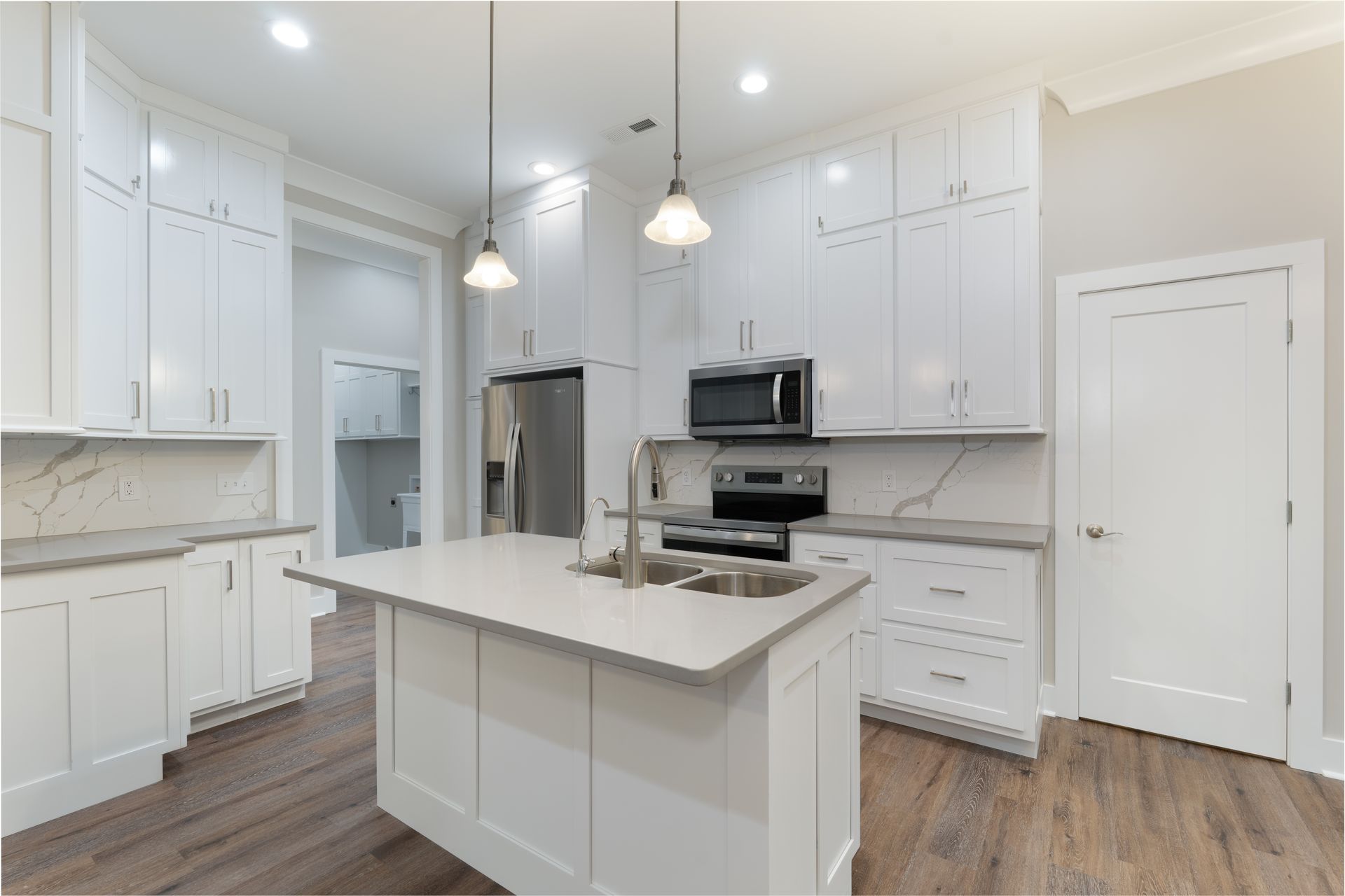 Modern white kitchen with island, stainless appliances, pendant lights, and wood-look flooring