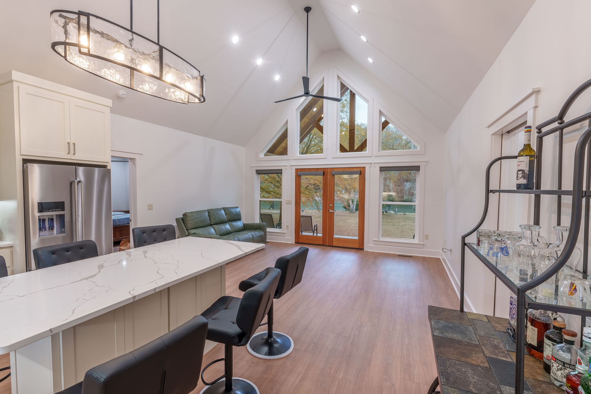 Modern open kitchen and living room with high ceilings, large windows, island, and curved staircase