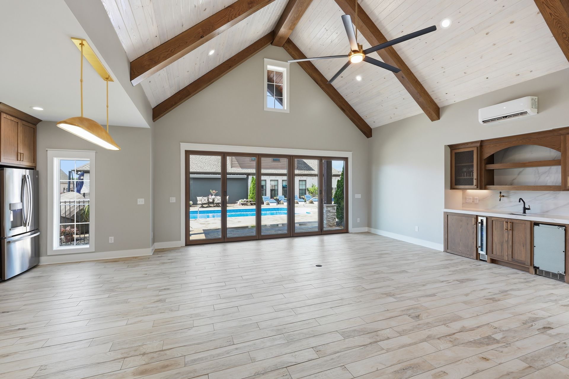 Bright open living room with vaulted ceiling, ceiling fan, fireplace, and large glass doors to a pool.