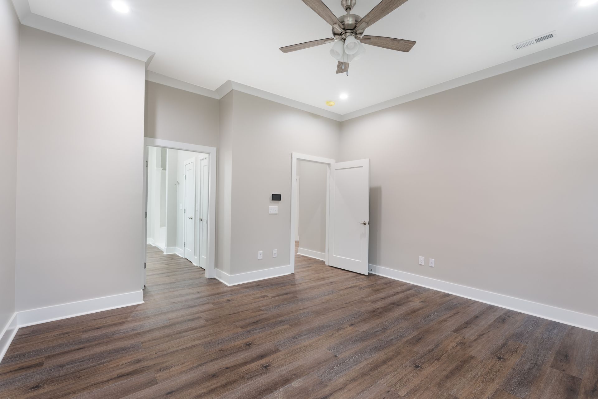 Empty bedroom with gray walls, wood-look floors, ceiling fan, and open closet doors